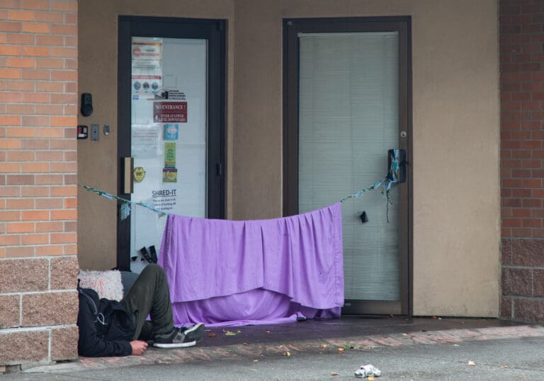 A man rests in a doorway on Unity Street next to a makeshift tent hung up by a rope.