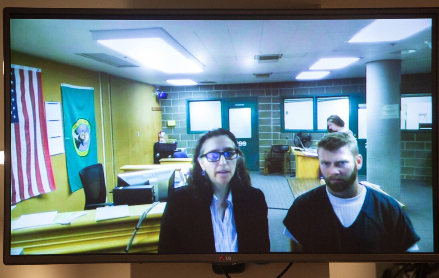 Brian Drake, right, appears for a hearing in a telecast from the Whatcom County Jail next to a helper speaking on his behalf.