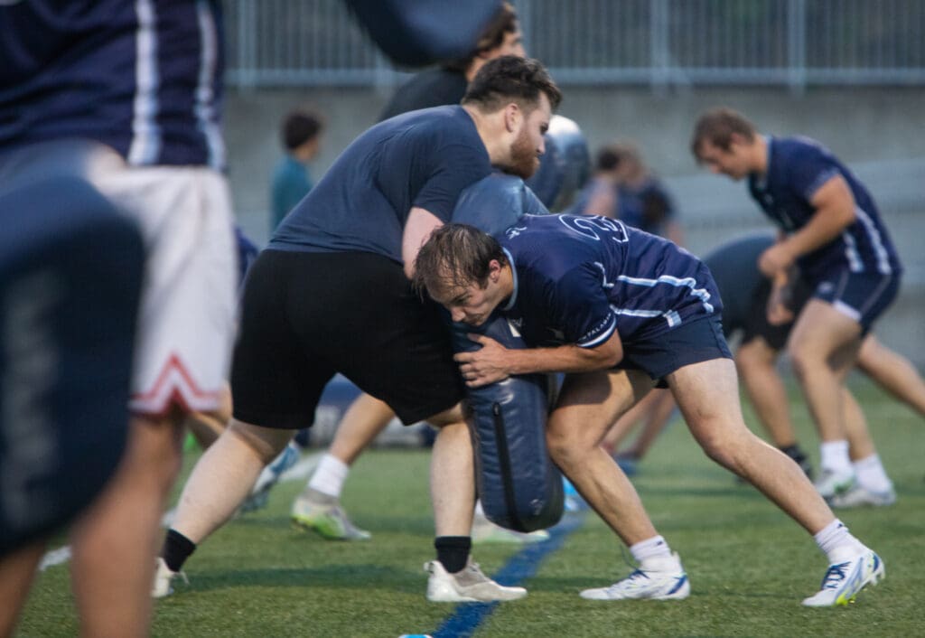 The Western Washington University rugby team running drills during practice has players tackle cushions held up by staff.