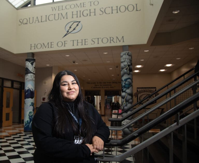 Juanita Villarreal stands near a wall with totem-designed columns that showcase Squalicum High School and their slogan.