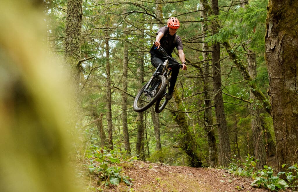 Talus Lantz midair with his bike in the dense forestry.