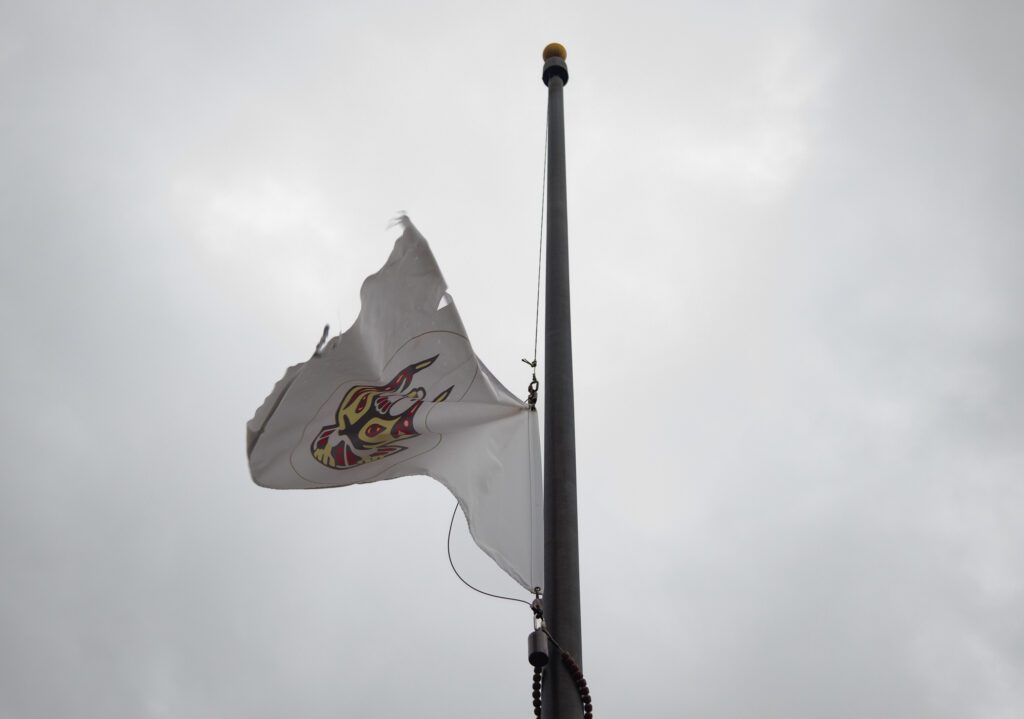 The Lummi Nation flag waves at half staff on a cloudy day.