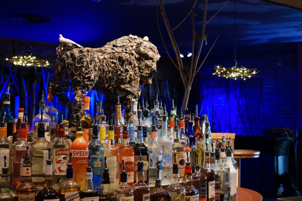 The iconic buffalo sculpture in the middle of the bar is adorned by two fake birds and surrounded by different various types of alcoholic drinks.
