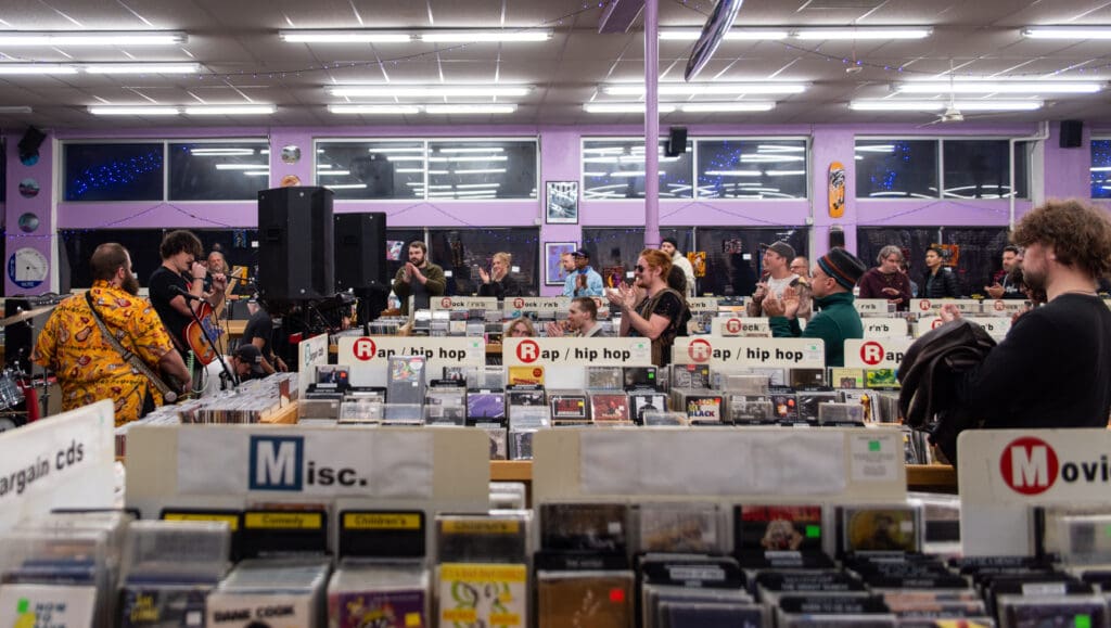 A crowd applauds Bellingham-based Smooth Kiwi inside the purple building of Ritual Records as they are surrounded shelves of records.
