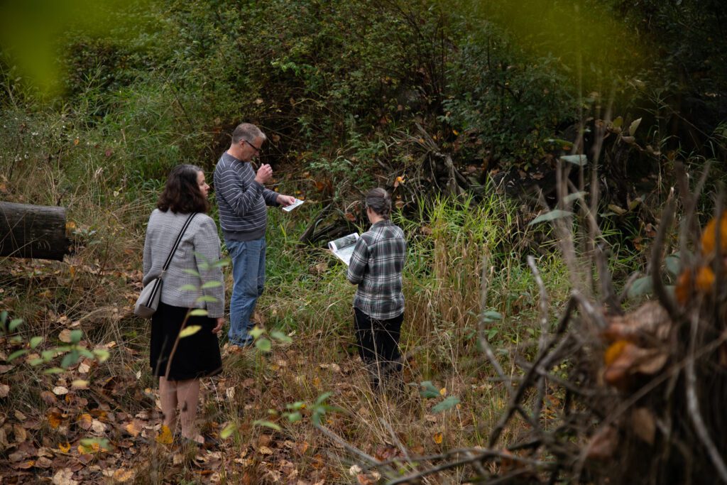 From left, Sen. Shewmake, Whatcom County Council member Todd Donovan and natural resources program specialist Becky Snijder van Wissenkerke stand in a stream channel as they look at their notes.
