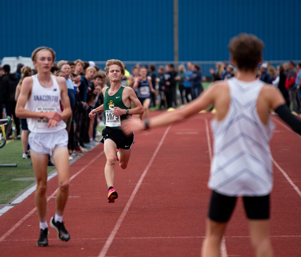 Sehome junior Heath Terry runs the final stretch to another runner who has their arms stretched wide.