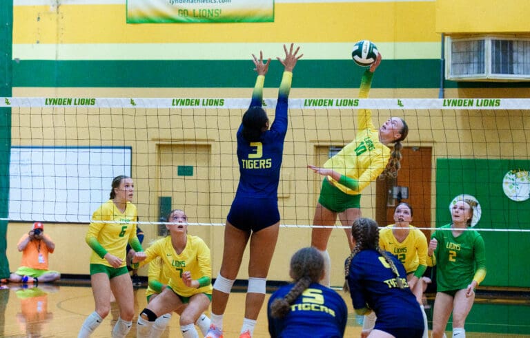 Lynden's Ashley Shumate (10) hits the ball over the net as a defender leaps to block the shot.