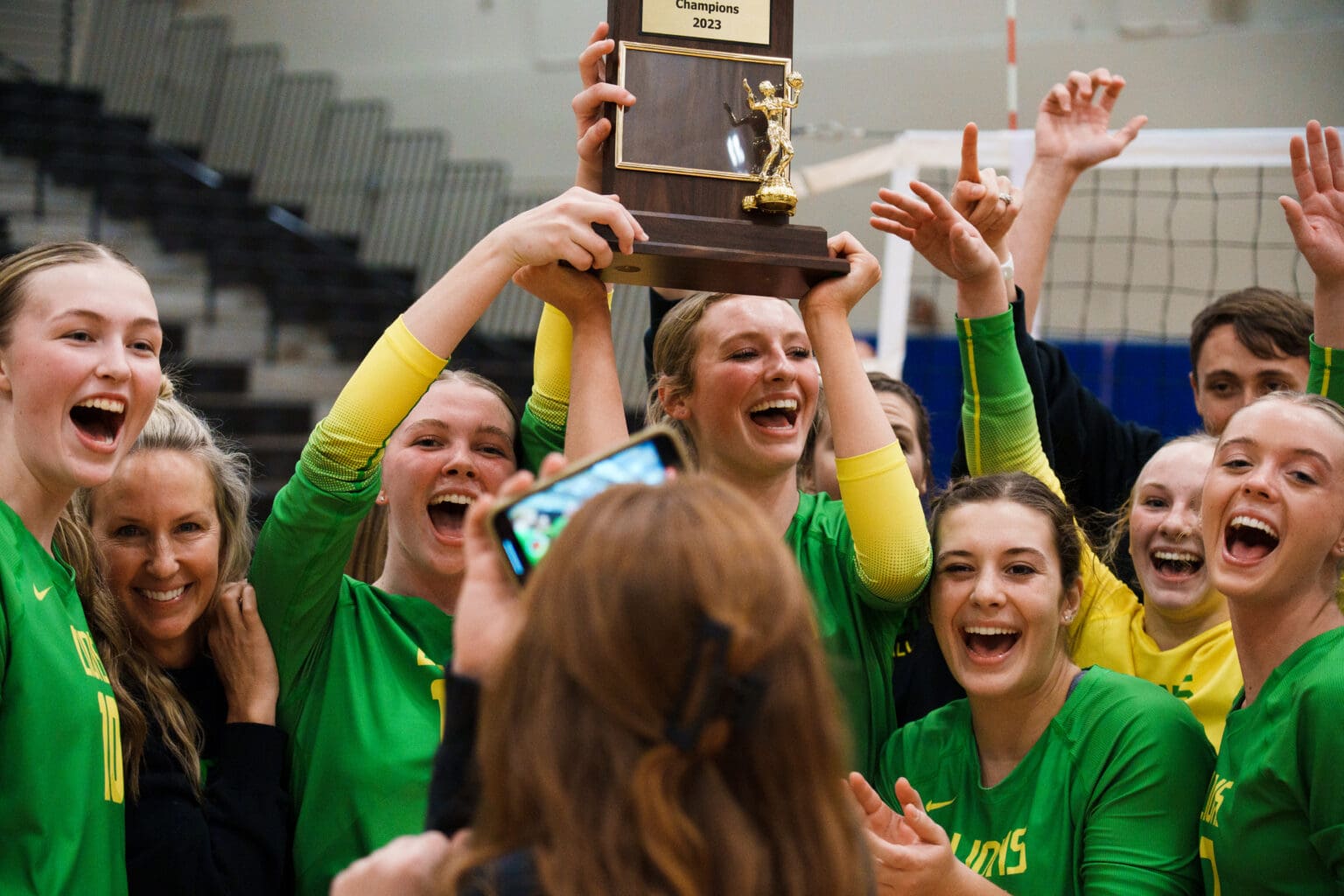 Lynden's Rian Stephan holds up the 2A District 1 championship trophy over her celebrating teammates.