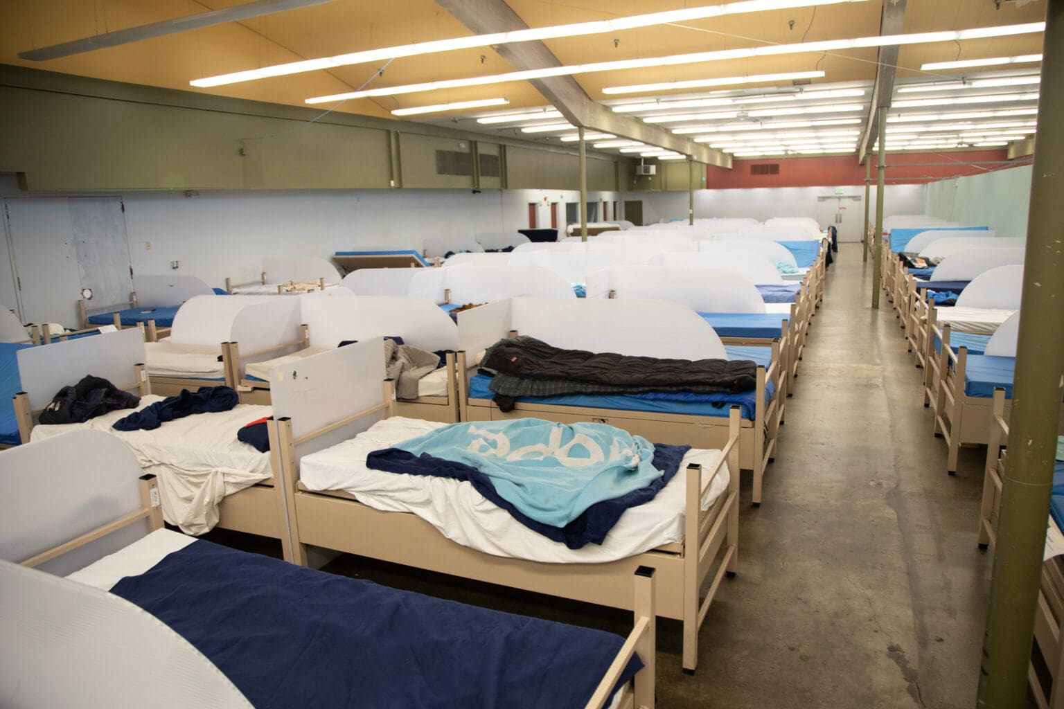 Beds with different comforters and blankets fill the men's dorm of the Base Camp shelter.