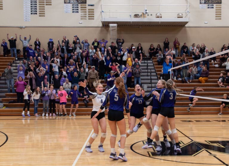 Nooksack Valley celebrates scoring a point as they yell and reach to embrace one another.