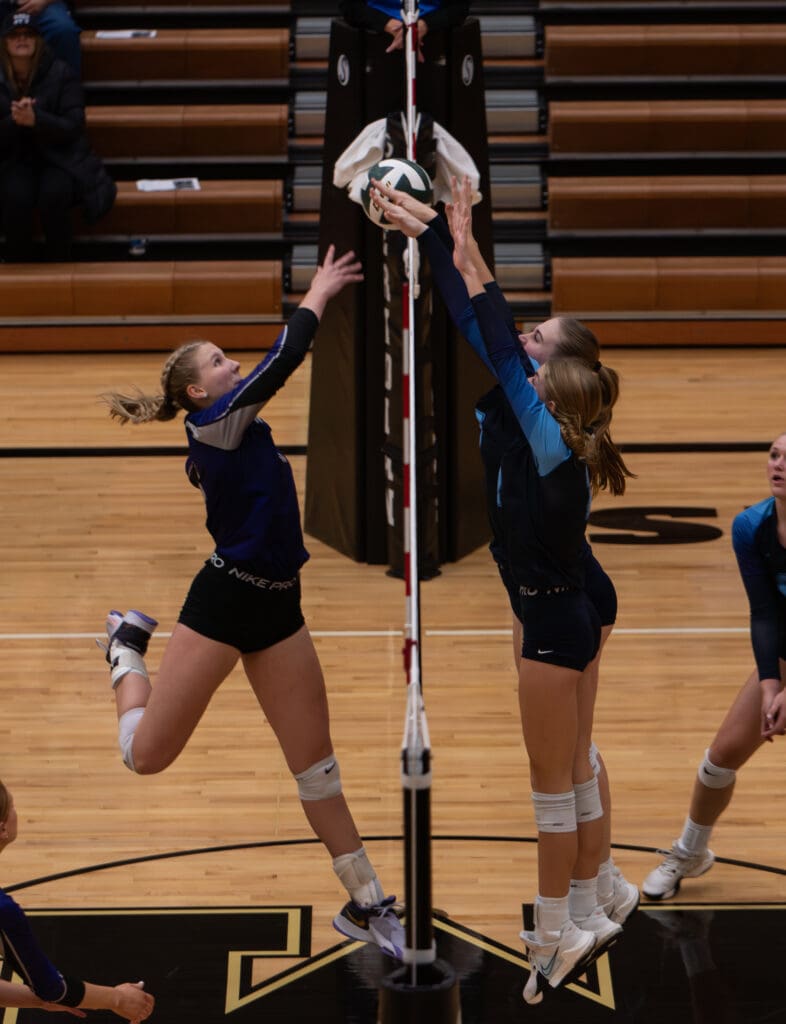 Tana Hoekema hits the ball over the net around Lynden Christian's blockers who are tiptoeing to try and block.
