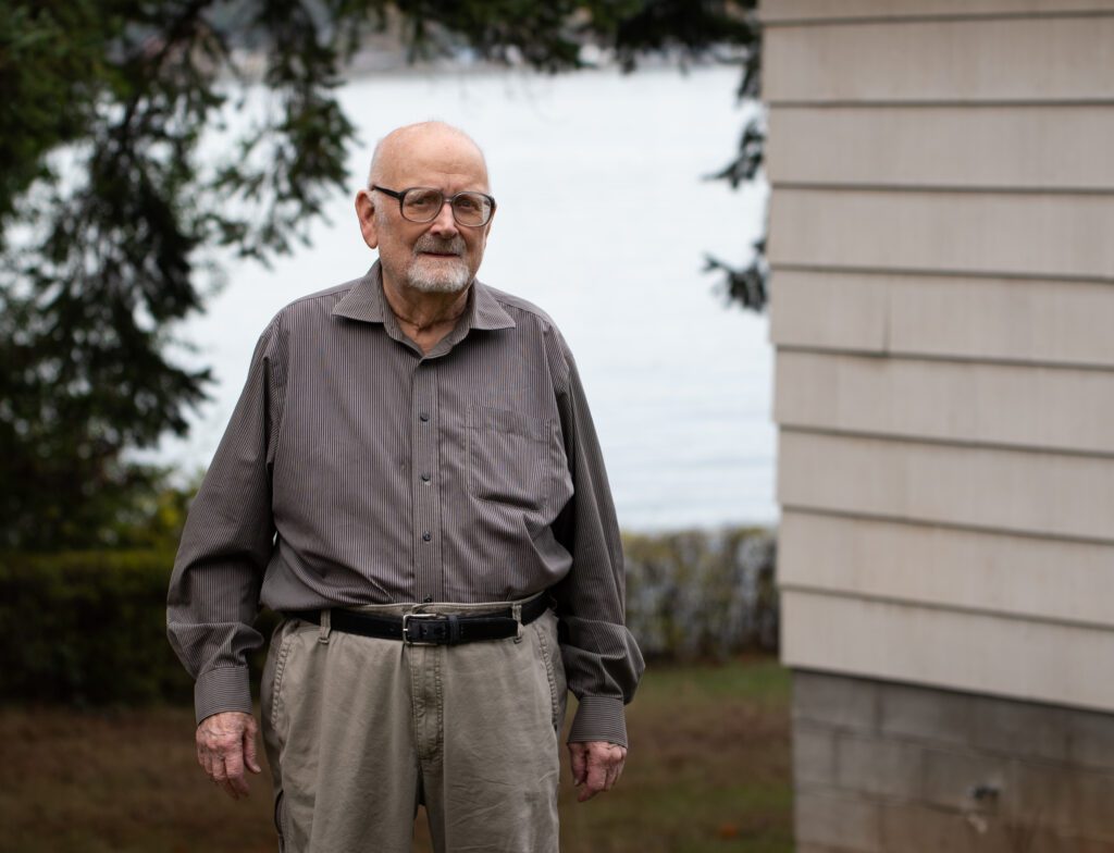 Paul Davis stands in his yard and next to his home on Lummi Island.