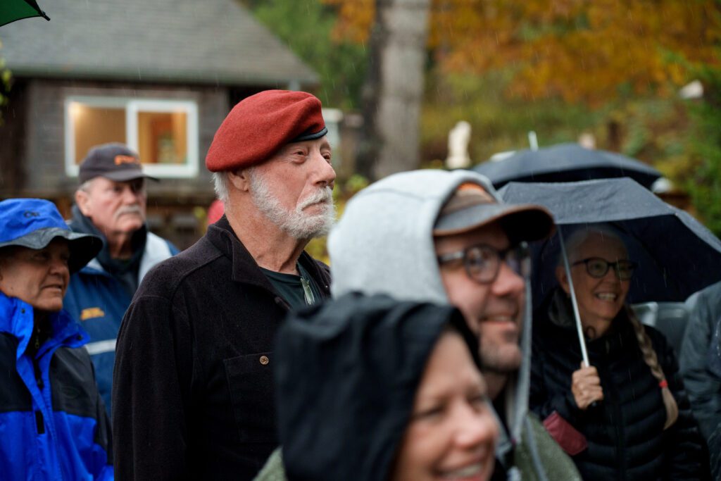 An attendee braves the rain while wearing a bright red beret as other attendees cover up with caps, umbrellas, and hoodies.
