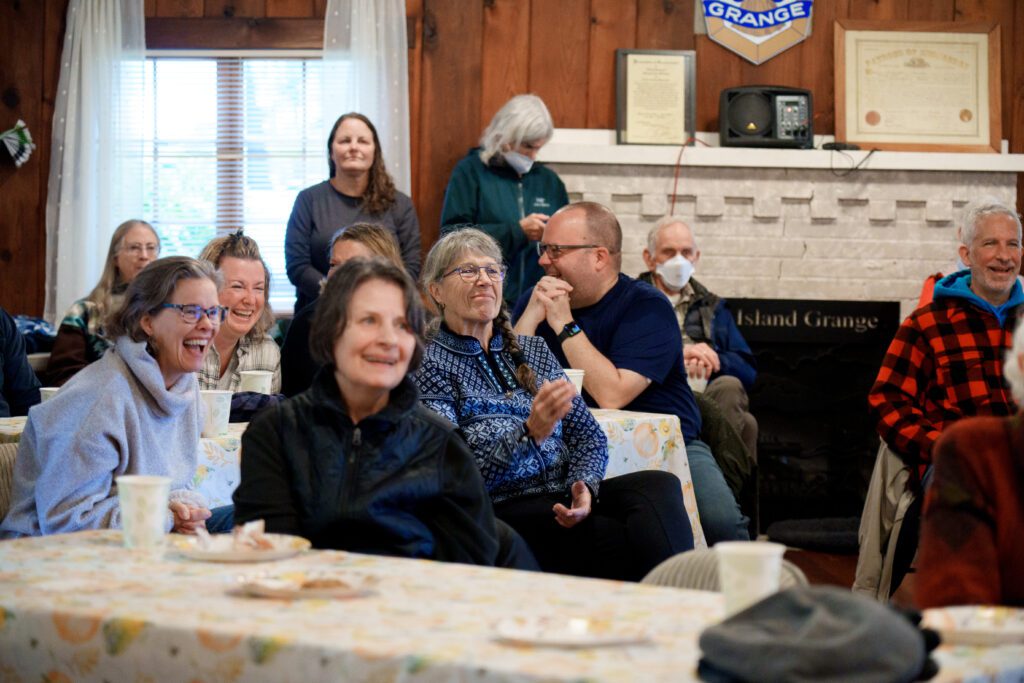 Attendees laugh during "story time" with Paul Davis inside The Grange building as they enjoy eating and listening.