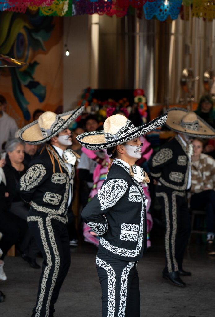 Dancers perform in front of a large crowd with all dancers dressed in matching attire and skull makeup.