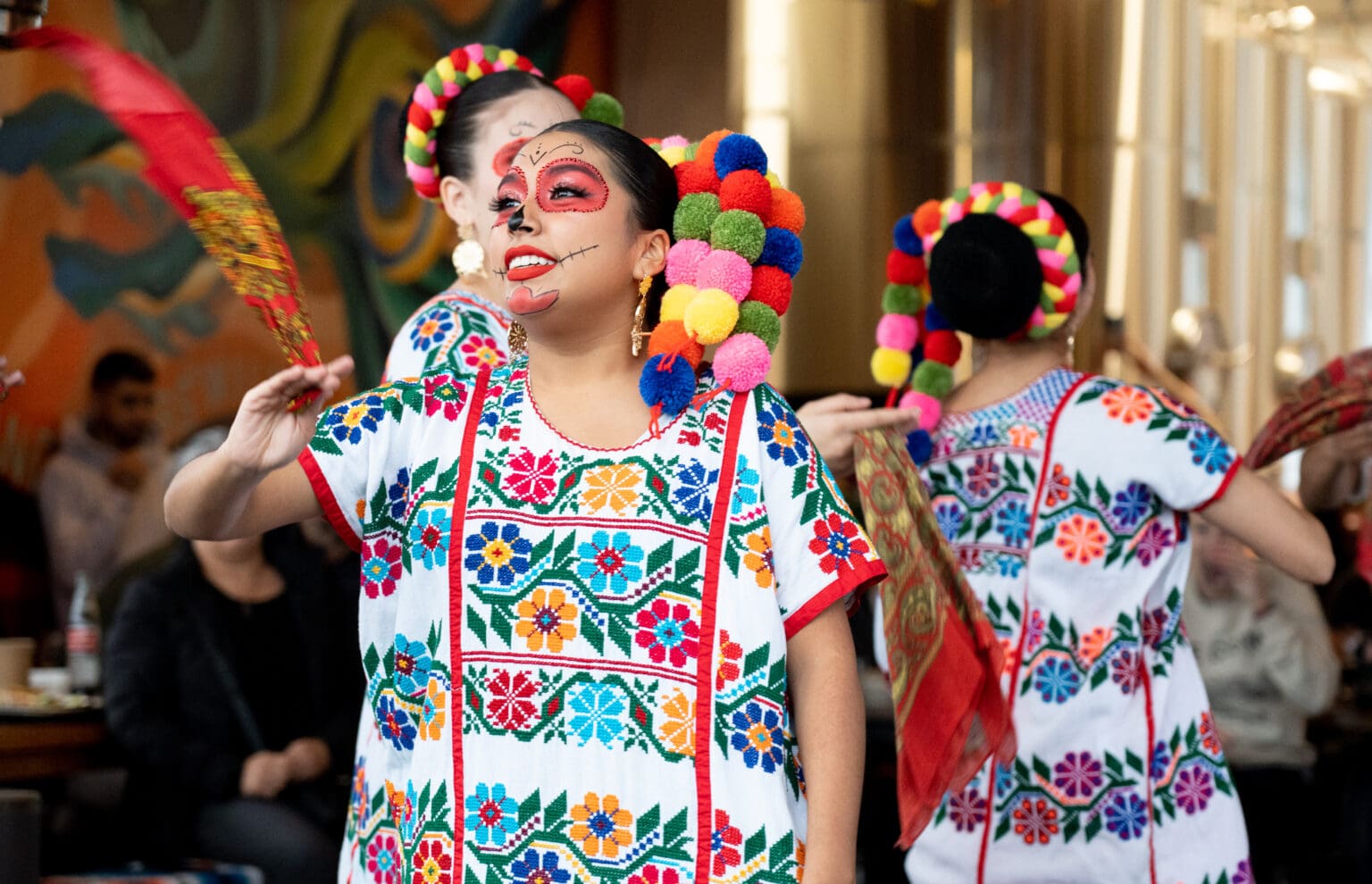 Dancer Arianna Gonzalez performs alongside other dancers dressed in colorful Día de los Muertos themed attire.