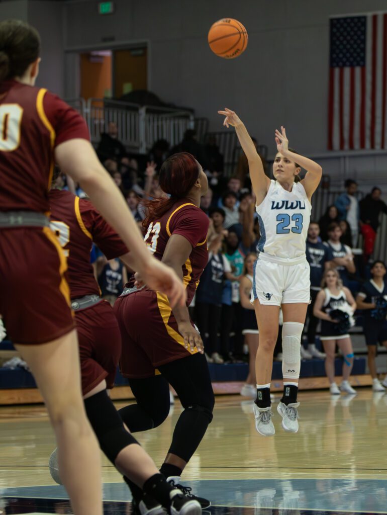 Mason Oberg shoots the ball as she leaps slightly off the floor to take a 3-pointer shot while defenders watch as they failed to reach her in time.