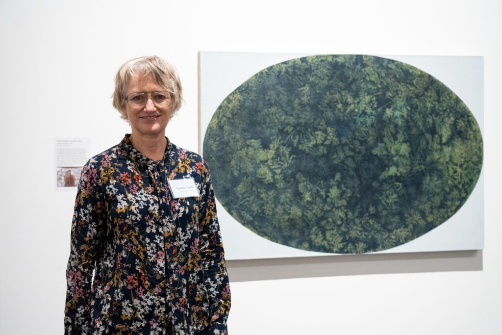 Bellingham-based artist Cynthia Camlin poses by her piece, "Sphagnum (Deep)," that is an oval forestry on white canvas.