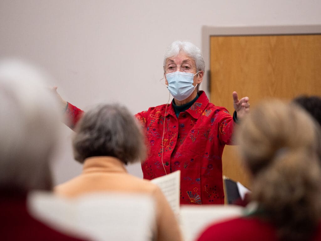 Whatcom Chorale Artistic Director and Conductor Deborah Brown gestures to the choir while wearing a mask.