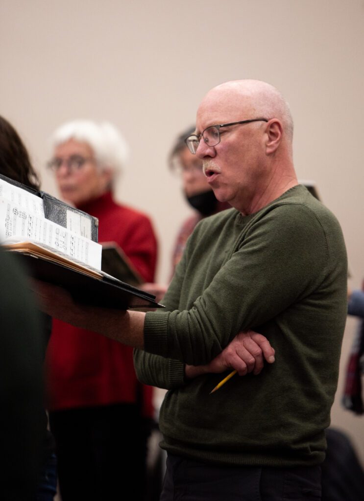 Whatcom Chorale President Eric Morgan sings a solo as he holds up a black binder holding music sheets and lyrics.