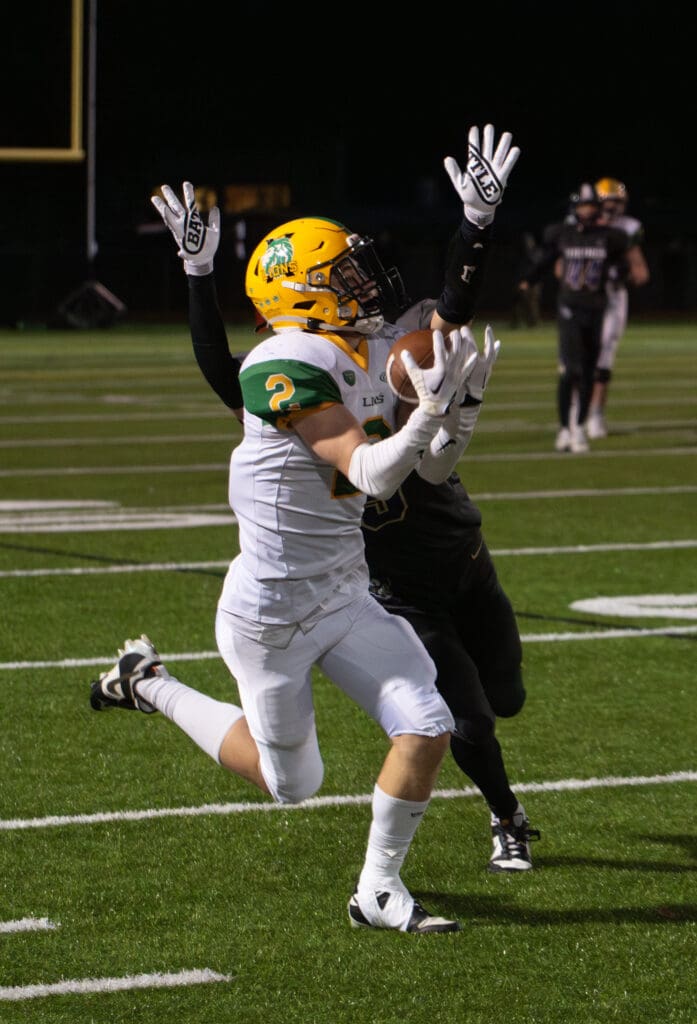 Lynden senior wide receiver Brady Elsner hauls in a pass while another player from the opposing team has his hands up in the air behind him.