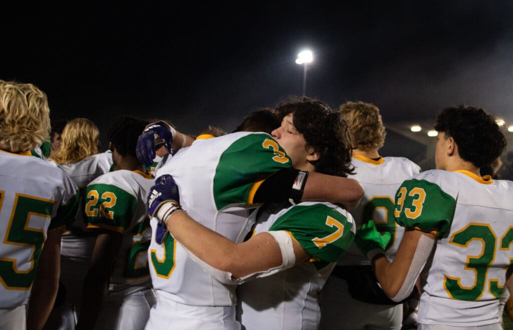 Lynden senior wide receivers Weston VanDalen (3) and Zach Welch (7) hug after the game surrounded by other members of his team.