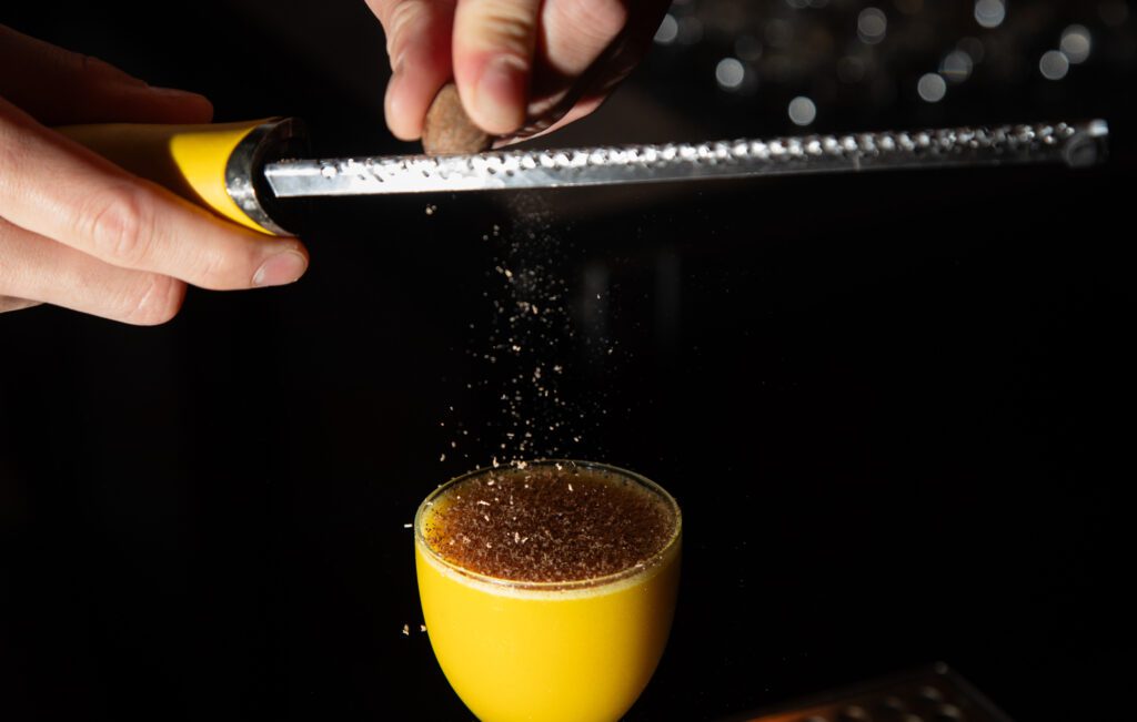 Bar manager Robbie Hagan grinds fresh nutmeg onto Carnal's drink Cheaper Than Saffron, a yellow drink with a bit of brown from the nutmeg on the top.