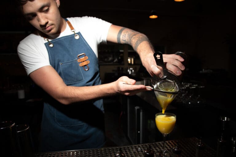 Carnal bar manager Robbie Hagan strains the drink Cheaper Than Saffron, a yellow drink, into a glass.