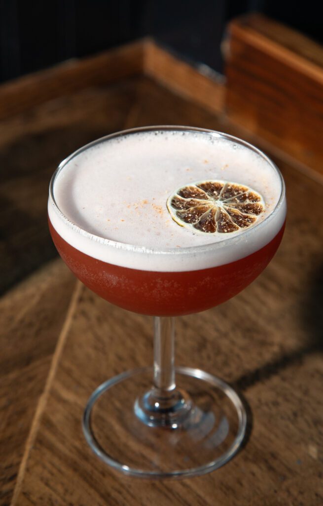 The Diving Woman from Redlight Kitchen & Bar is a red drink served with a light pink foam and garnished with a slice of dehydrated lime.