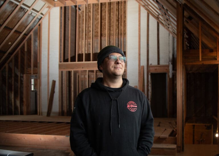Nazar Gamdysey stands in the gutted sanctuary from Bellingham's Ukrainian Evangelical Church wearing black attire and a black hoodie as they smile for the camera.