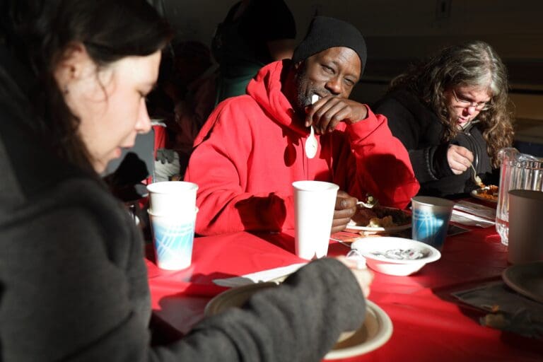From left, Jewel Couture-Voyce, JD Conner and Evynn Parsons eat and chat at a red table with plastic plates, utensils, and drinks.