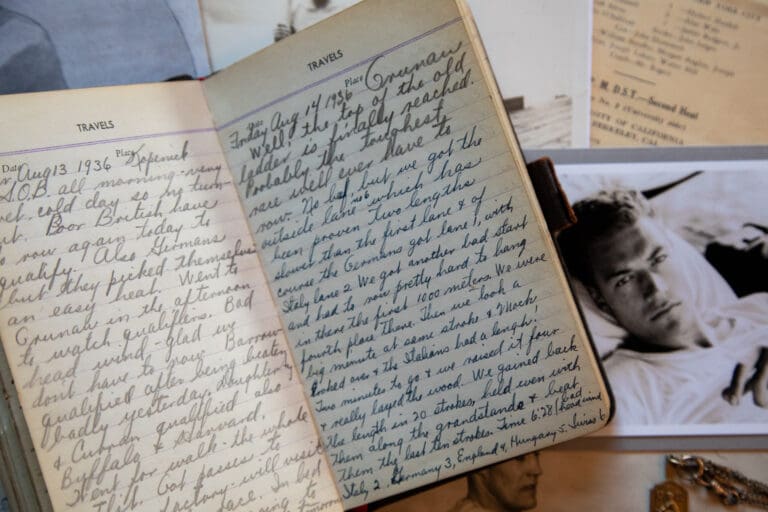 An old travel diary is filled with cursive writing. A picture of a young man and other memorabilia sits below.