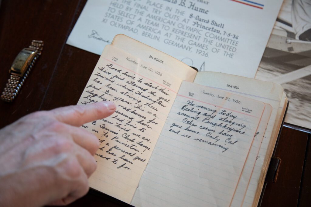 A man's finger points to cursive text in an old diary.