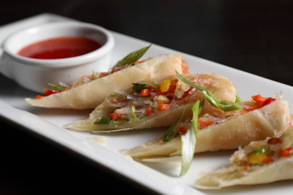Spring rolls cut and filled with cabbage, bell peppers, squash, mushrooms and rice noodles are served with a side of sweet and sour sauce.