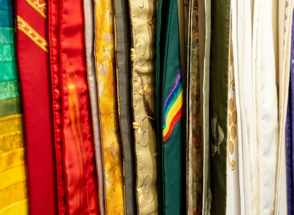 A colorful variety of pastor stoles hang, one with a rainbow on it.