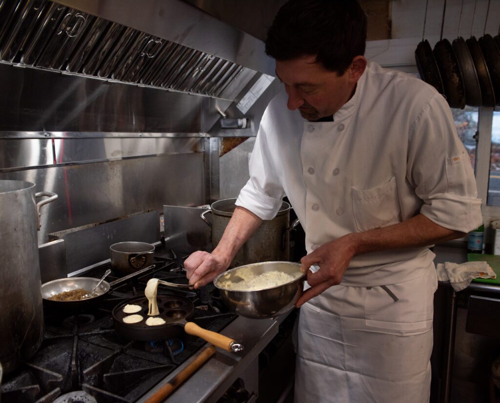 Chef de Cuisine Nate Hansen ladles batter into a pan with specific circular molds.