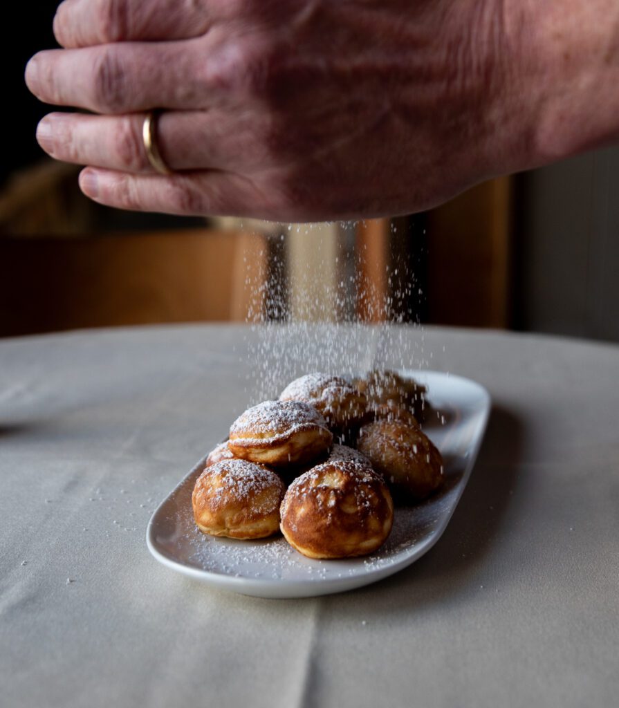 Nate Hansen dusts powdered sugar onto the Æbleskiver served on a white plate.