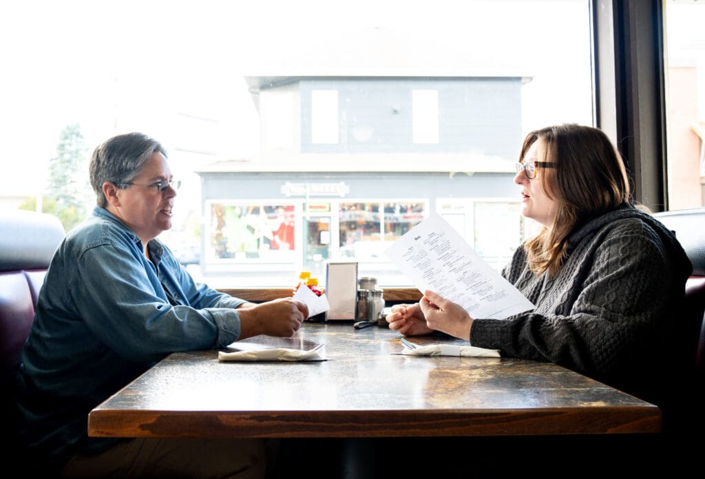 Two women sit at a restaurant table and hold menus as they talk.