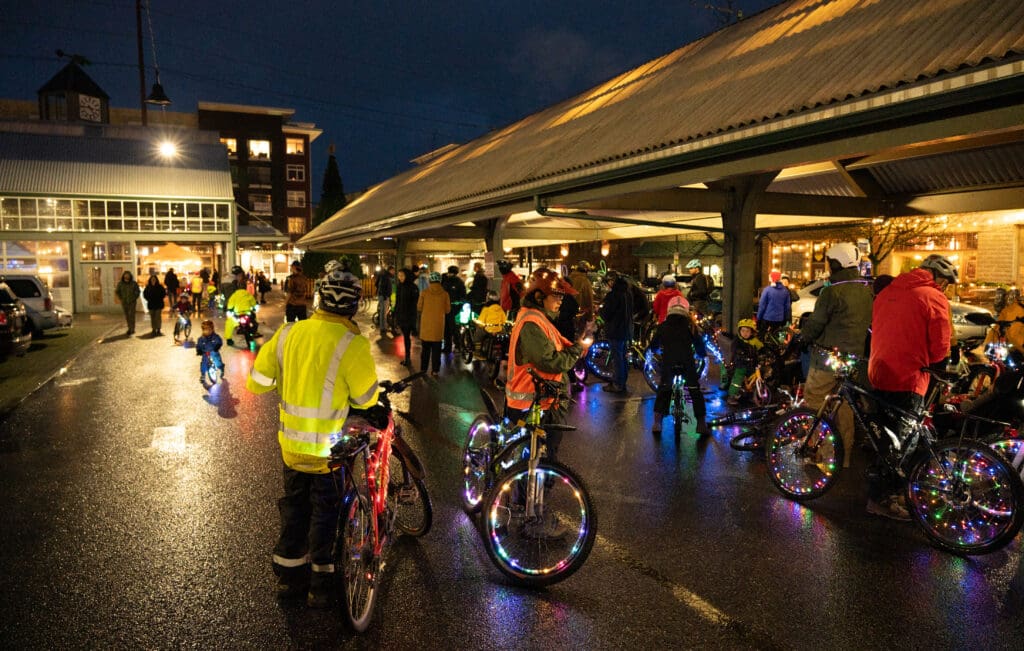 Nearly 75 cyclists of all ages corral in Depot Market Square at dusk before departing, all the bicycles are decorated in multicolored lights along their wheels.