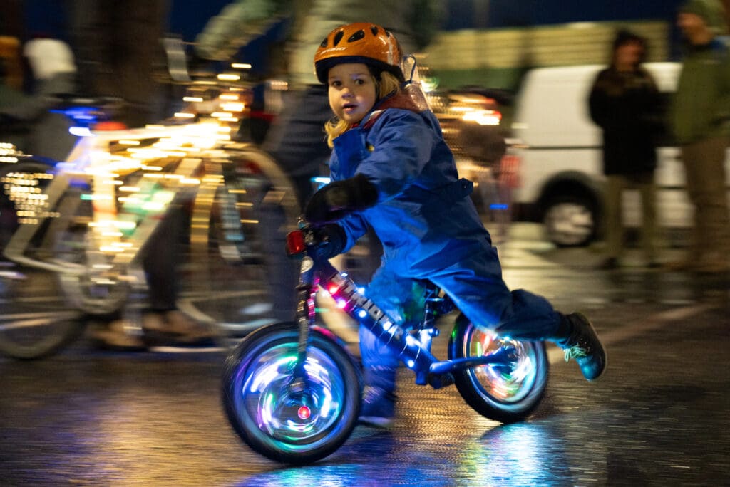 Leo Boyd, 3, rides his birghtly lit bike weaaring a full blue outfit and an orange bicycle helmet.