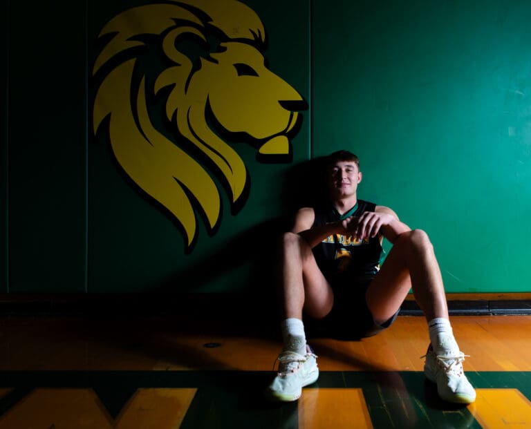 Brant Heppner sits against the green baseline pads while leaning against the dark green wall with a golden lion head next to him.