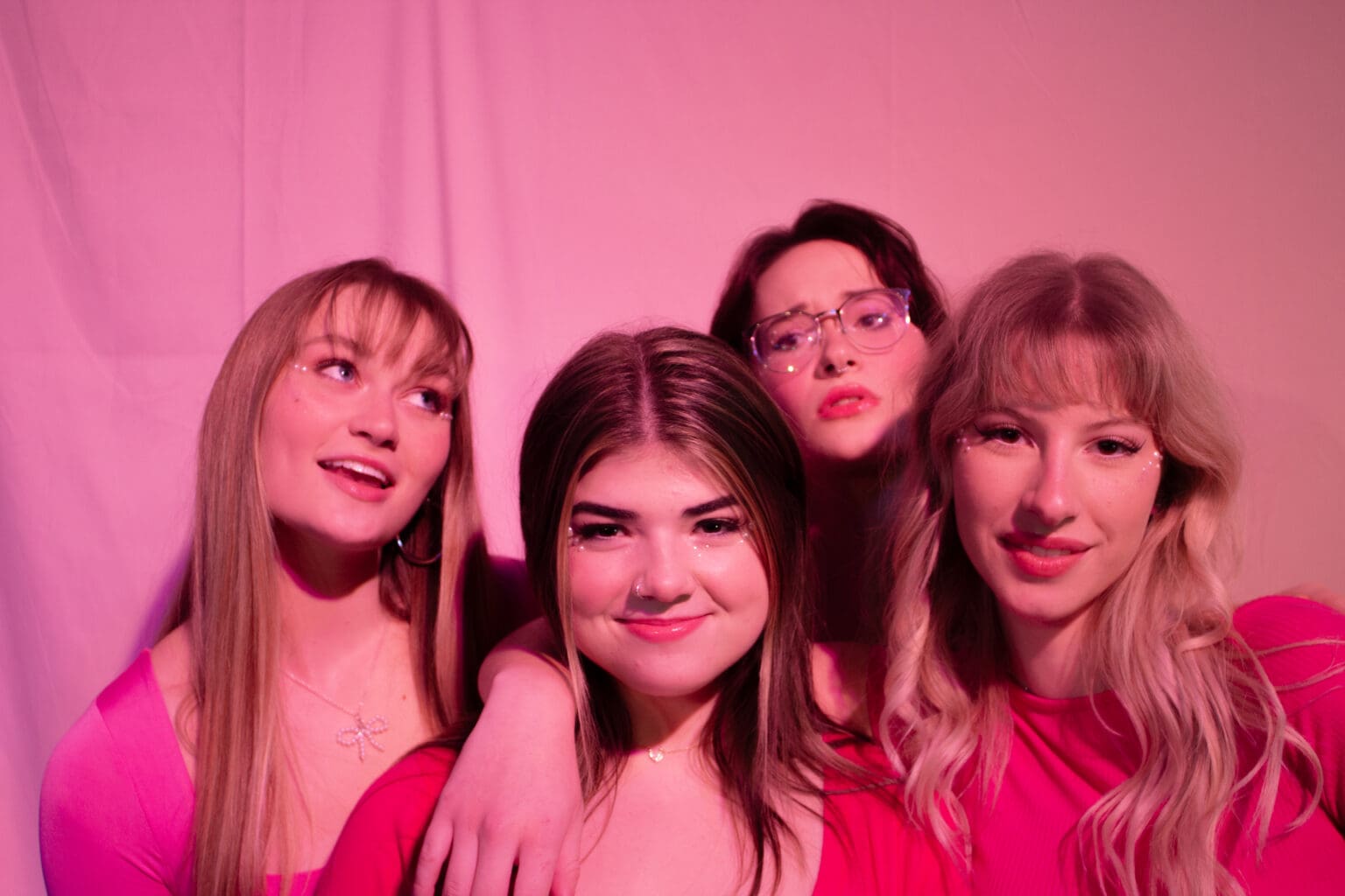 The cast of "Mean Girls: The Musical/High School Edition" posing for a photo underneath a bright pink light.