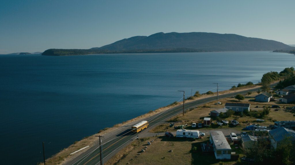 An aerial view of a school bus driving along the coast of a large body of water.