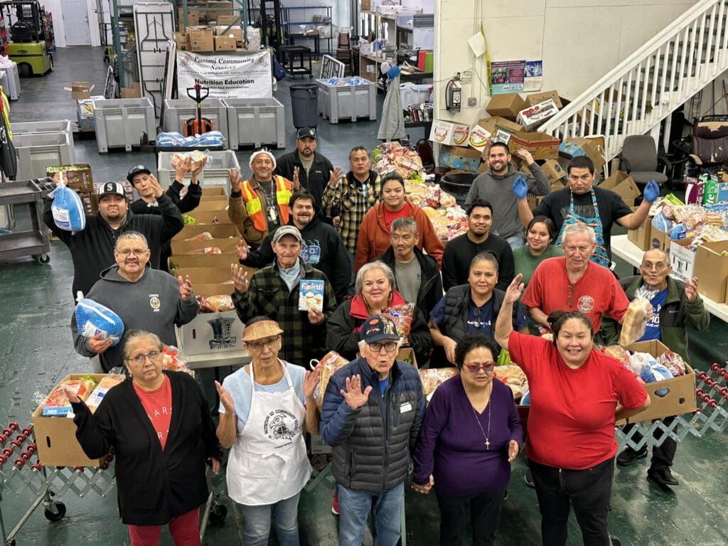 The Lummi Commod Squad look up to the camera with big smiles as they prepare Thanksgiving baskets.