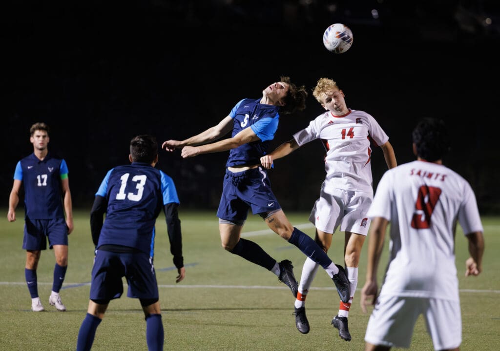 Western Washington University's Ryan Rotter leaps in the air with another player to head the ball as other players watch.