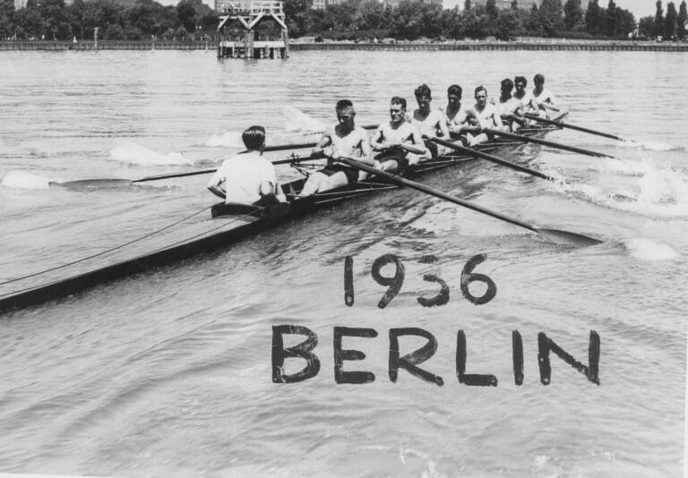 Shirtless young men row in a boat on the lake. Written on the photo says "1936 Berlin."