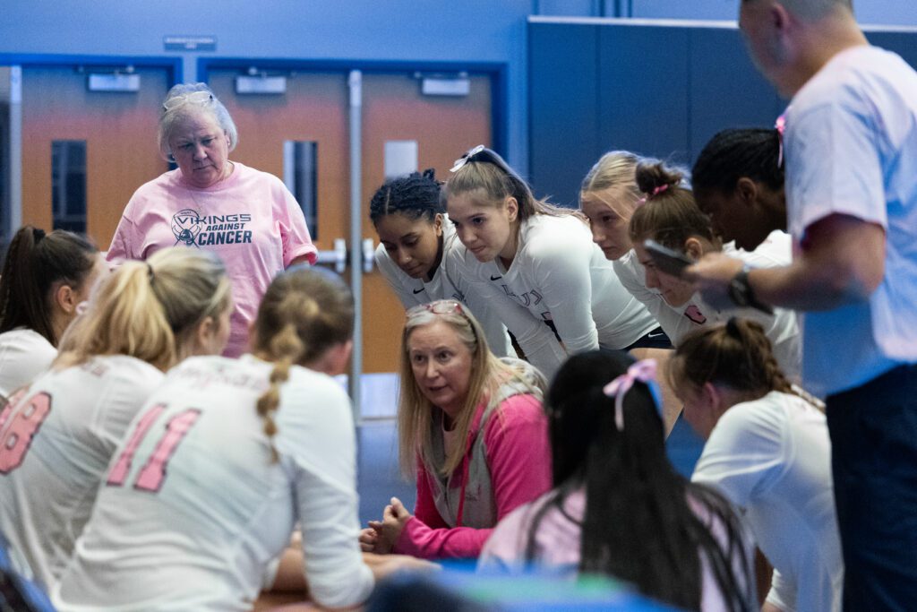Western Washington University volleyball coach Diane Flick-Williams kneels down to talk to her team who has her surrounded in a close huddle.
