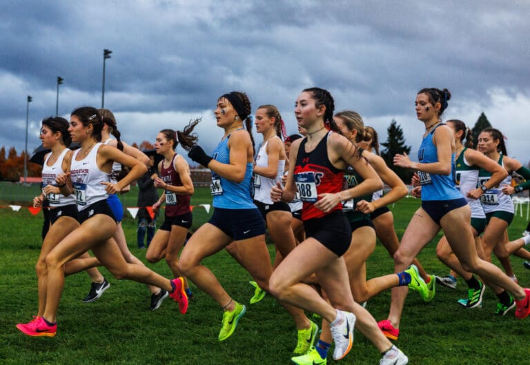 Western Washington University's Ila Davis, left, and Ashley Reeck run amid other competitors with cloudy skies in the background.
