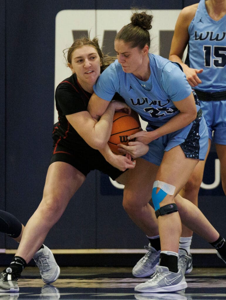 Western Washington University's Maddy Grandbois tries to get the ball out of Central Washington University player's hands as another player watches from behind them.