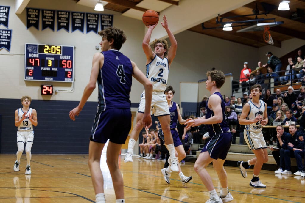 Lynden Christian’s Dawson Bouma leaps into the air to take a shot as other players and spectators watch.